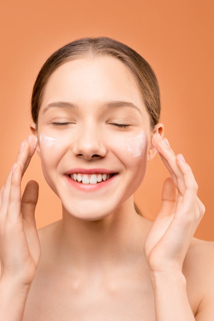 A cheerful woman applies face cream as part of her skincare routine, promoting health and beauty.